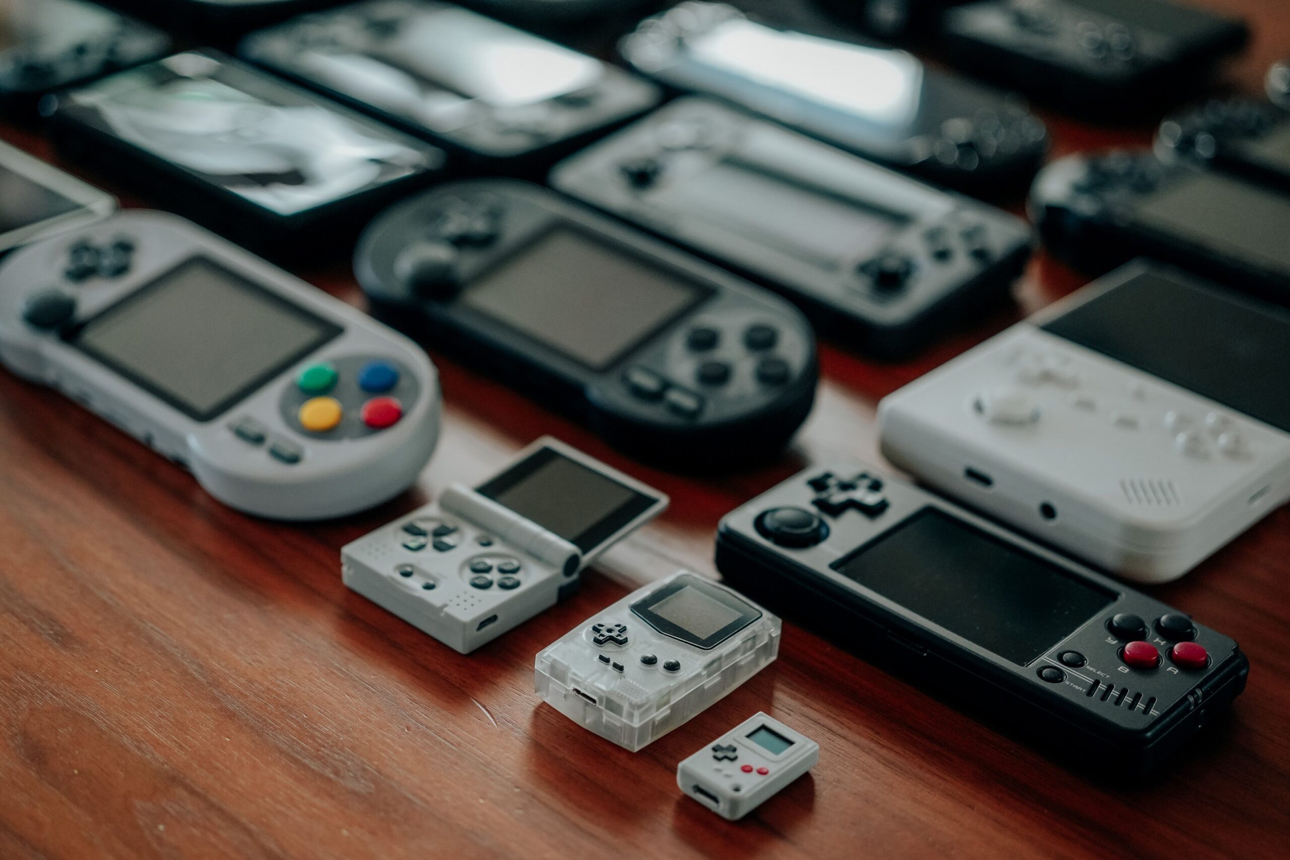 Collection of retro handheld consoles like the Game Boy, Game Boy Advance and PSP displayed on a wooden surface