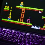 Laptop displaying a retro video game with a neon-lit keyboard in a dim room