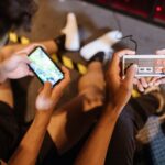 Teenagers playing mobile and retro video games indoors with a controller